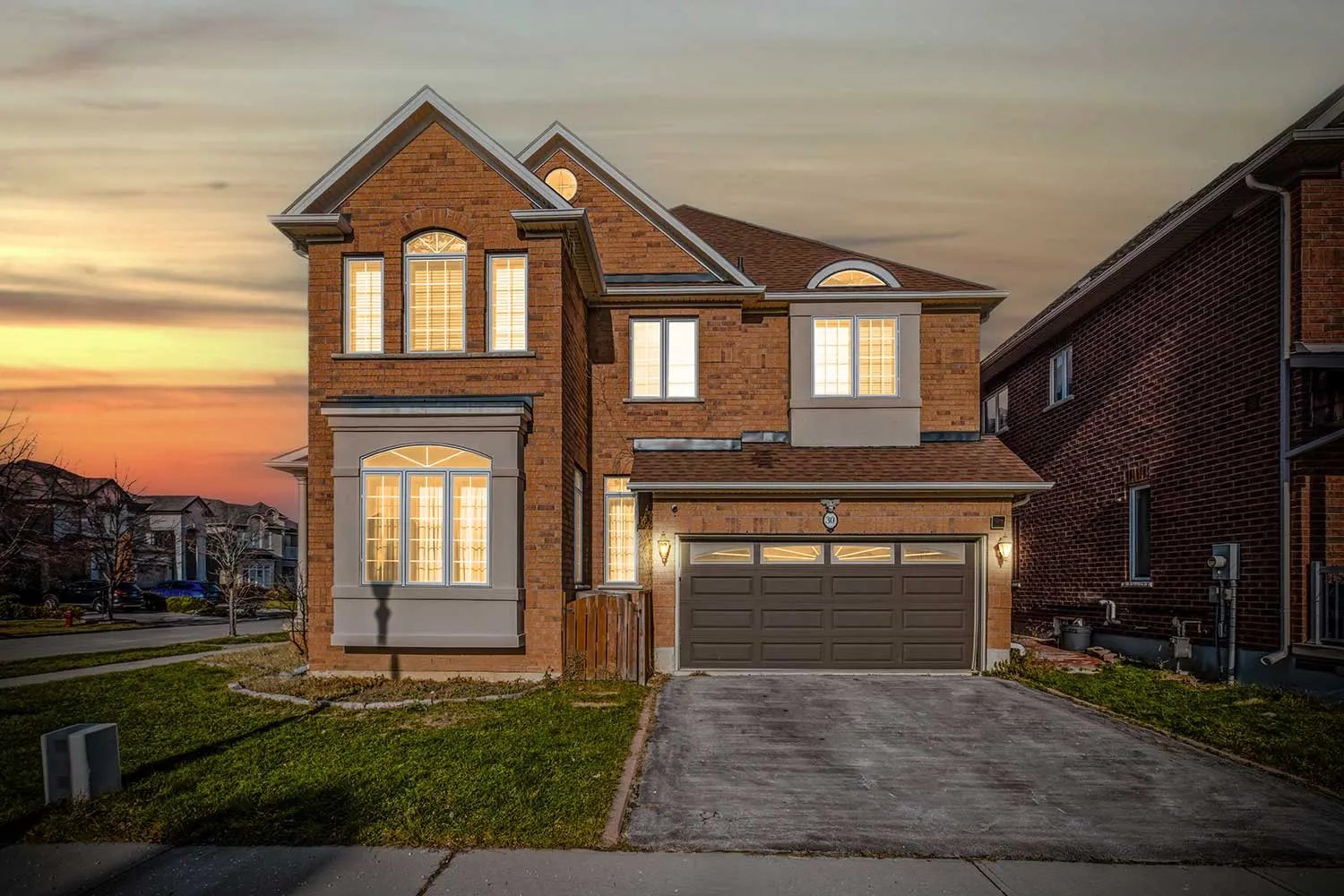 Digital twilight exterior photograph of a brick family home with warm interior lighting, by RCG Canada