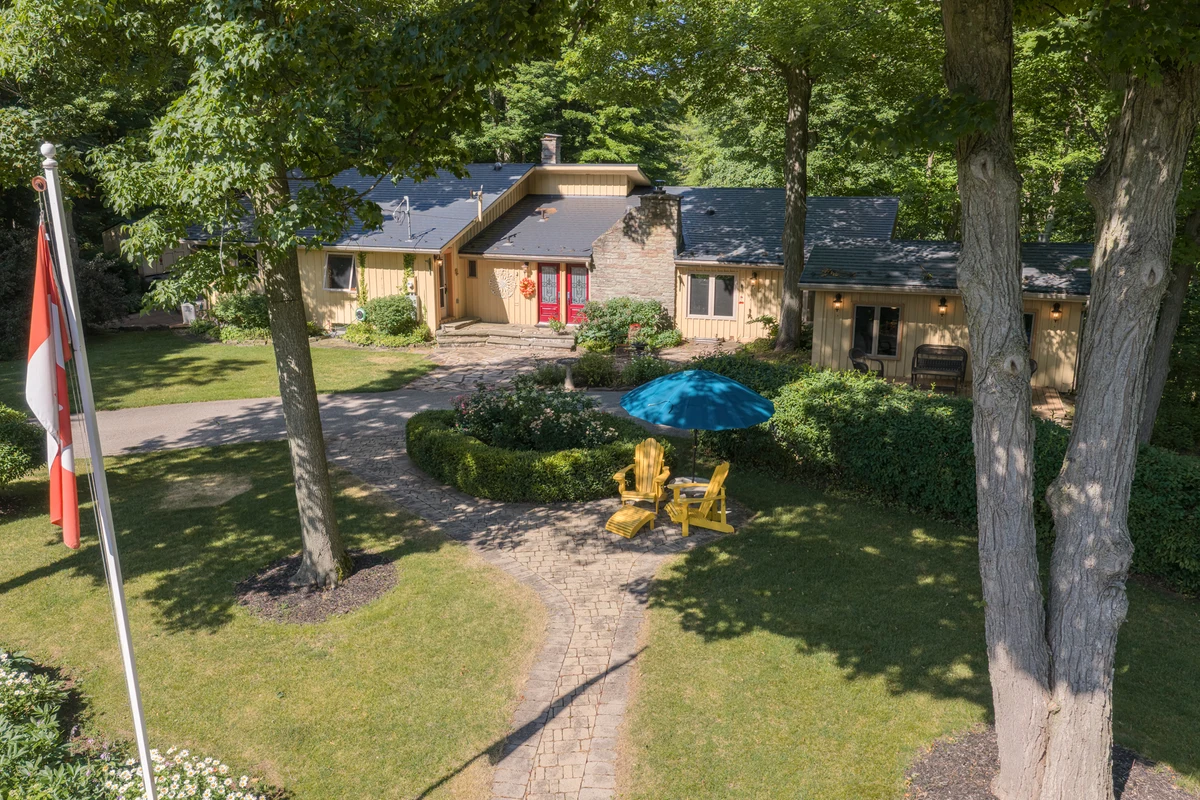 Aerial drone photograph of a Heritage Road estate home with its lawn, flagpole and garden seating among the trees. RCG Canada real estate photography