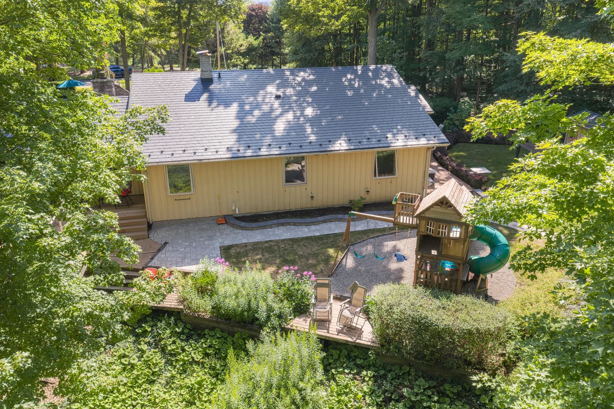 Low aerial drone photograph of a Heritage Road home’s rooflines and patio framed by surrounding woodland. RCG Canada real estate photography