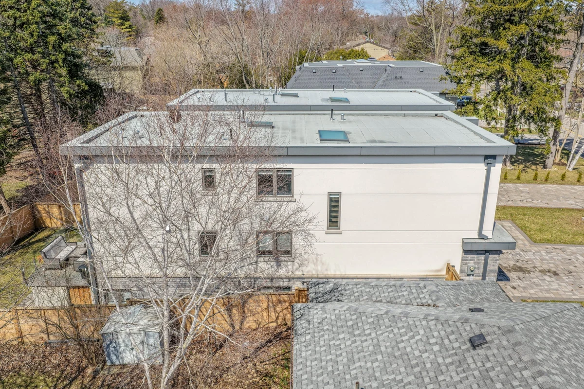 Aerial drone photo of a flat modern roofline and side elevation of a Mississauga property, surrounded by mature trees. RCG Canada real estate photography