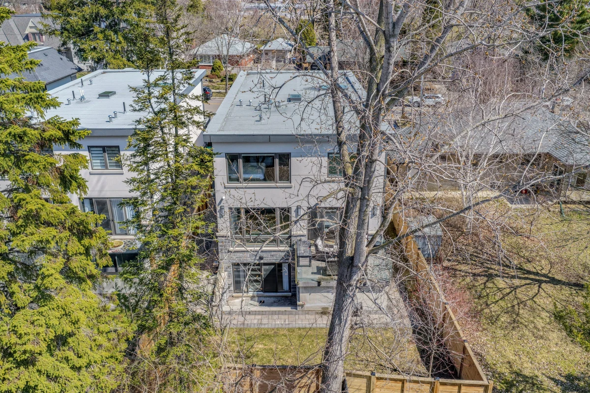 Aerial drone view of a modern Mississauga home's side elevation and multi-level glass balconies, framed by tall trees. RCG Canada real estate photography