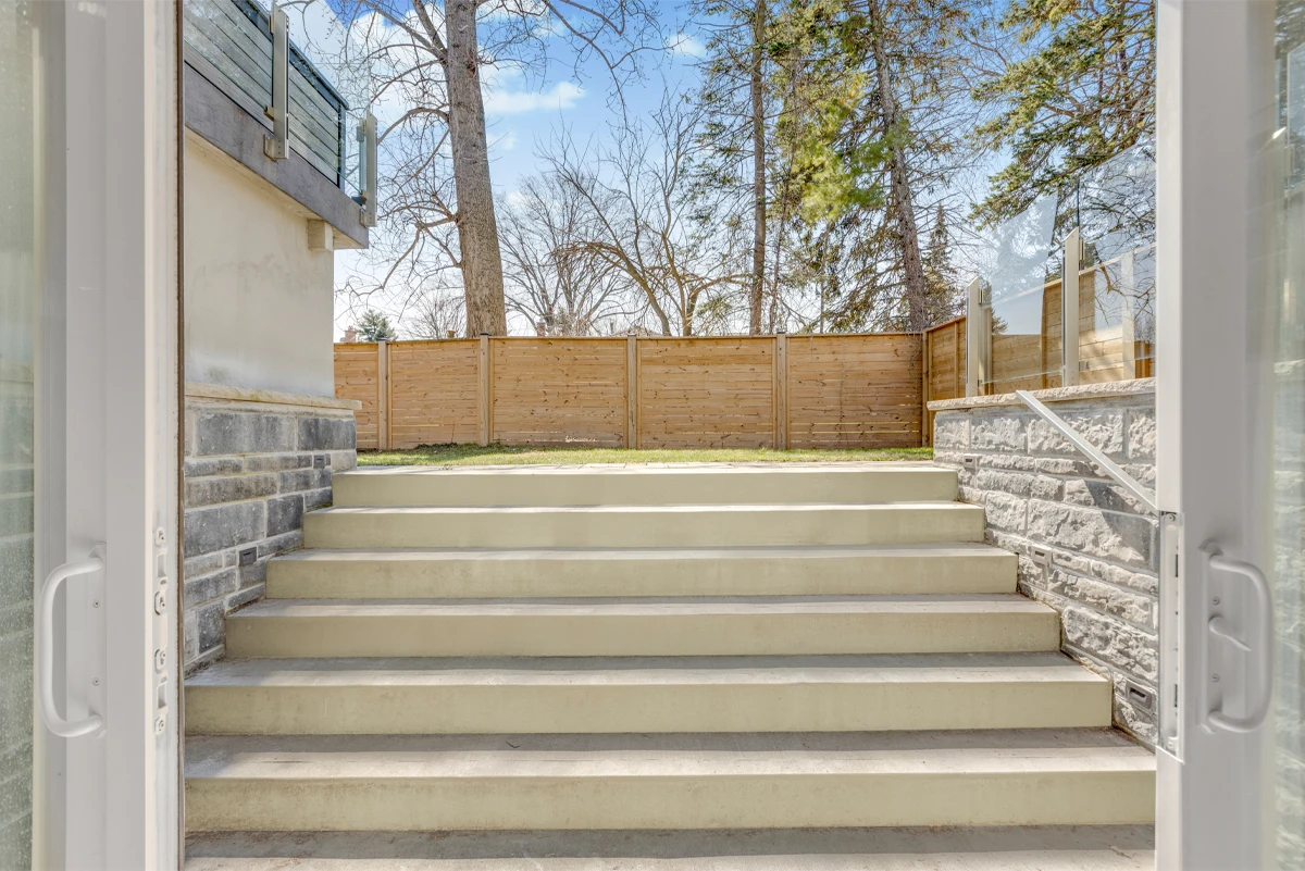 View from a lower-level walkout up wide concrete steps to the fenced backyard - RCG Canada
