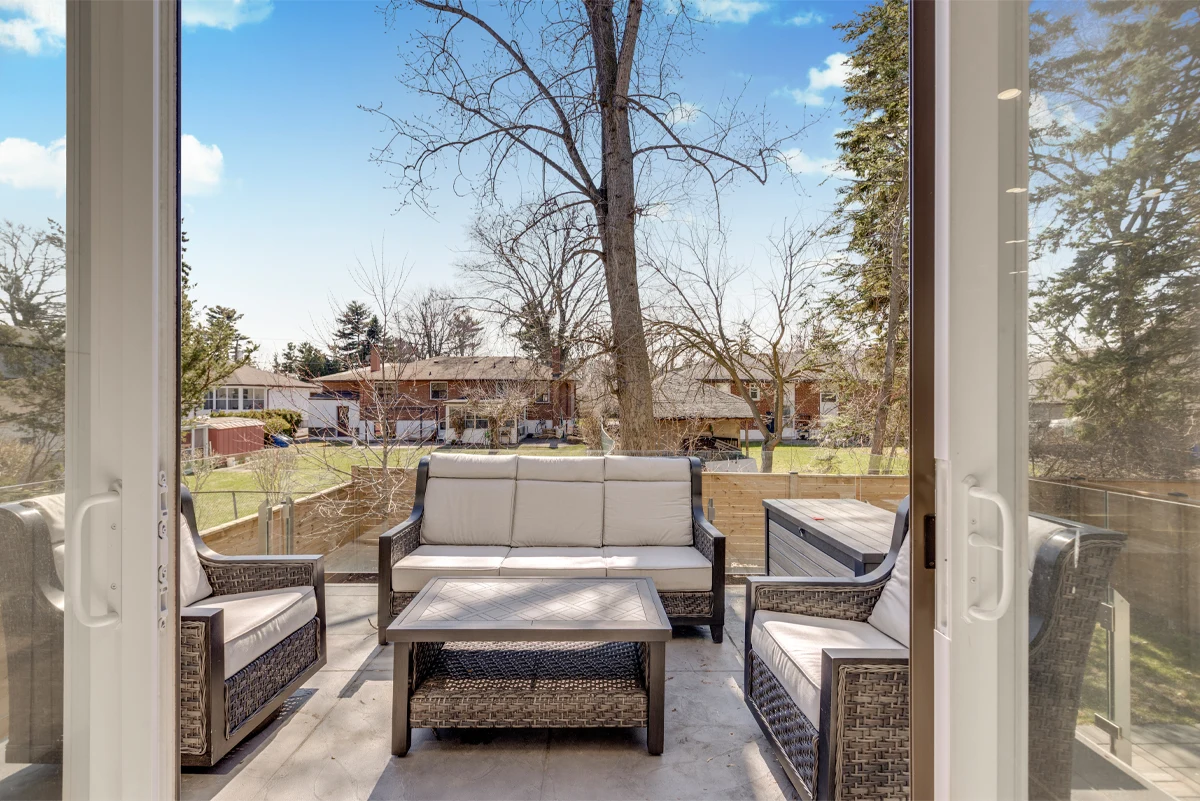 Rear terrace of a Mississauga home framed by open patio doors, wicker lounge seating and glass railings overlooking the treed backyard. RCG Canada real estate photography