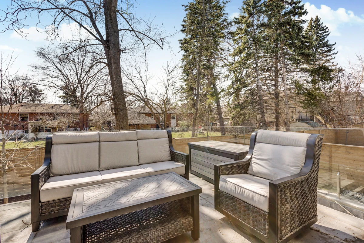 Outdoor lounge seating and storage bench on the glass-railed rear terrace, mature trees behind - RCG Canada