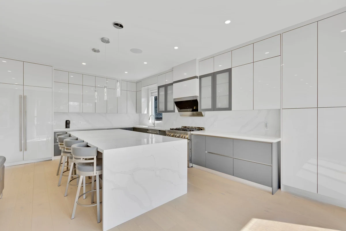 High-gloss kitchen with a quartz waterfall island, glass-front cabinetry and gas cooktop in a Mississauga home. RCG Canada interior photography