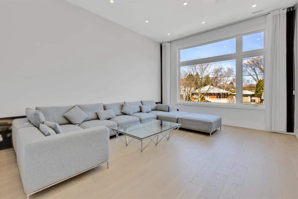 Upper-level family room with a pale grey sectional beside a wide picture window - RCG Canada
