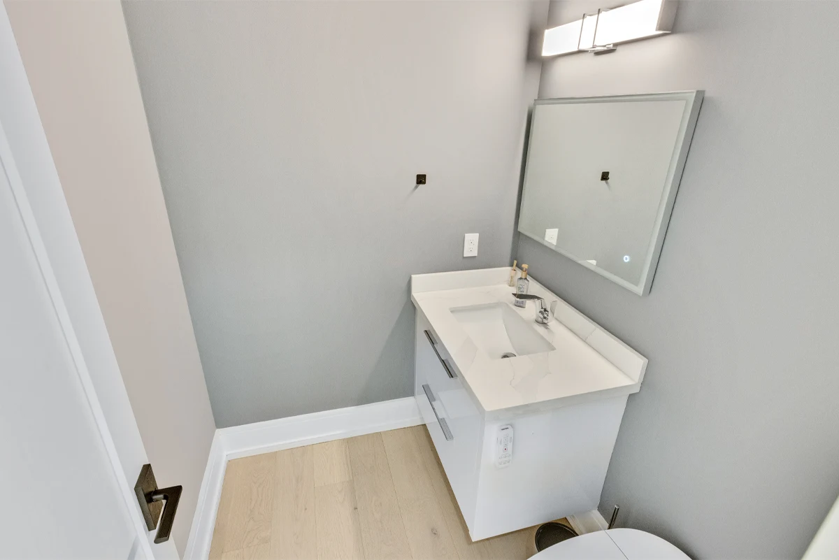 Powder room with a floating white vanity, quartz counter and backlit mirror in a Mississauga home. RCG Canada interior photography