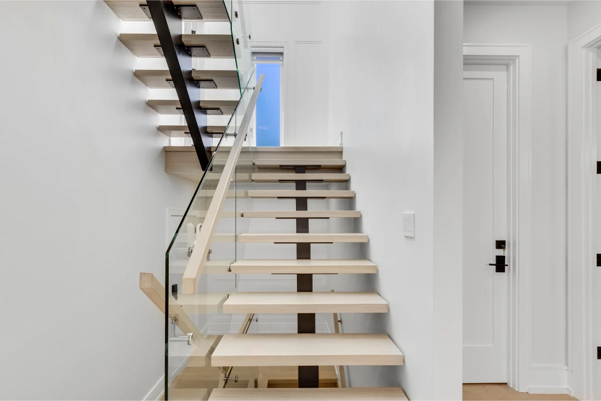 Floating white-oak staircase with a steel stringer and frameless glass railing, lit by a tall side window in a Mississauga home. RCG Canada interior photography