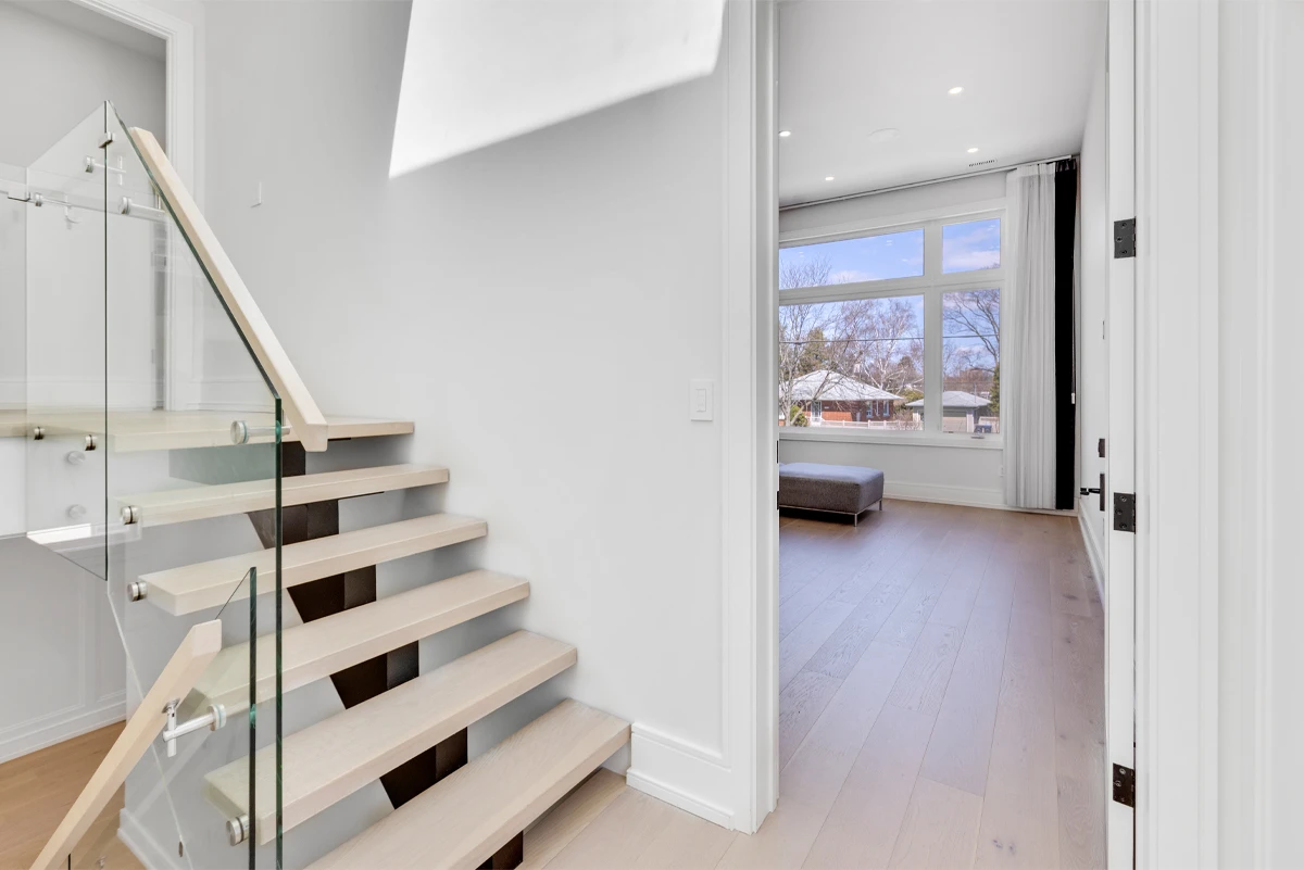 Floating staircase and upper landing opening onto a bright bedroom with wide-plank flooring - RCG Canada