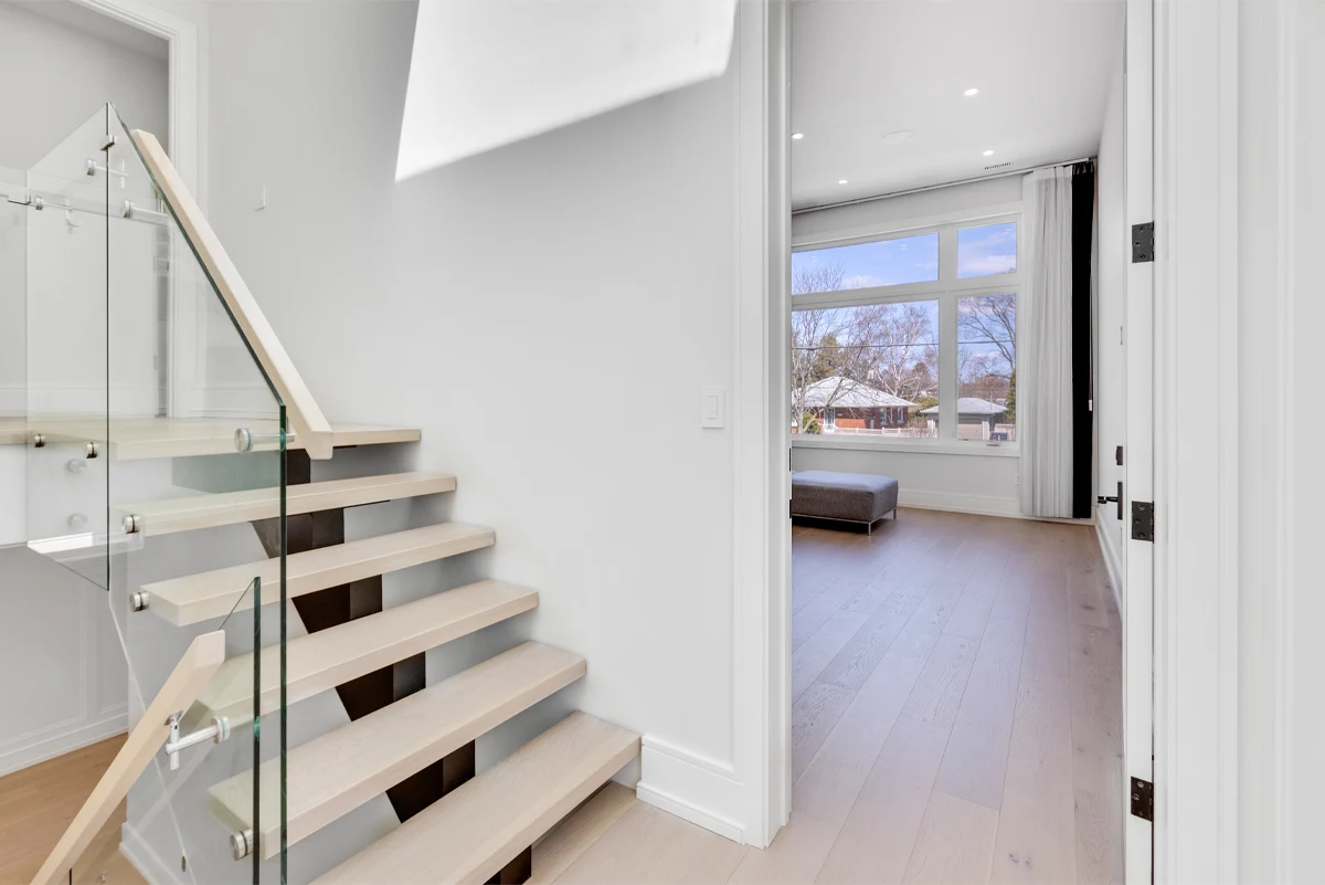Floating staircase and upper landing opening onto a bright bedroom with wide-plank flooring in a Mississauga home. RCG Canada interior photography