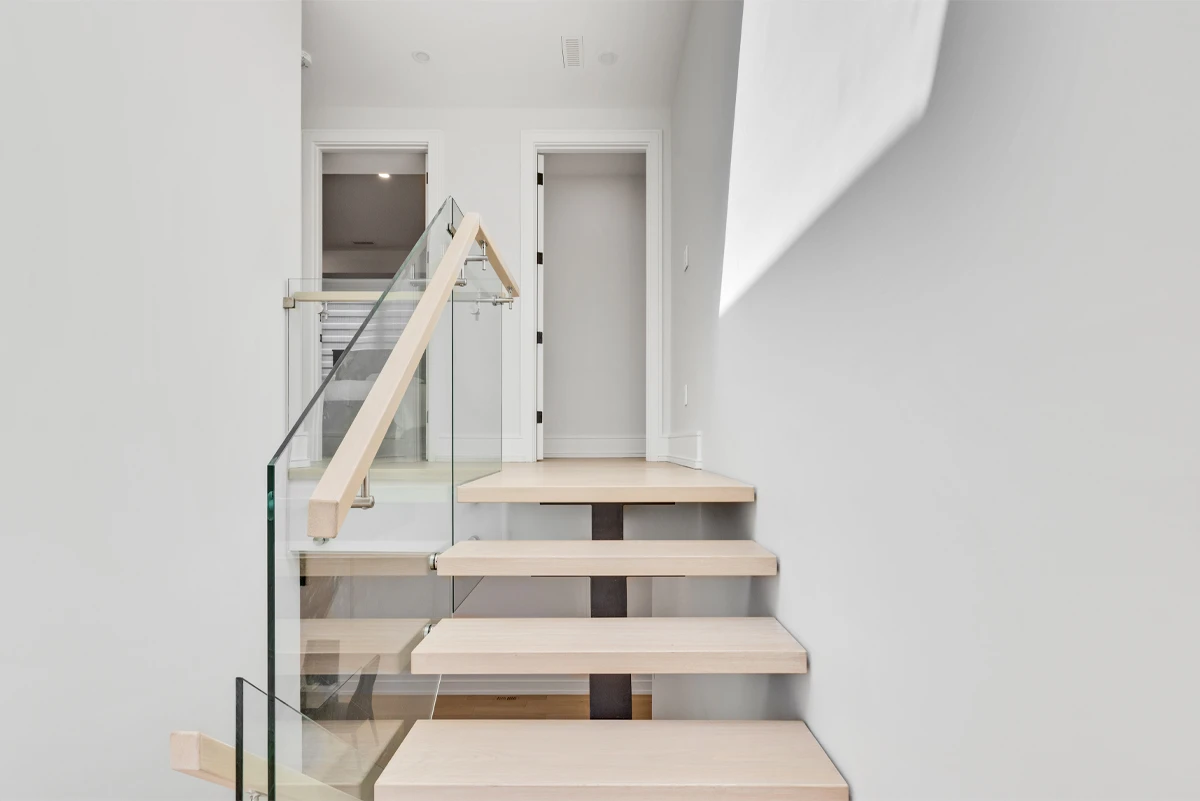 Staircase landing with glass railing and white-panelled doors under a skylit ceiling - RCG Canada