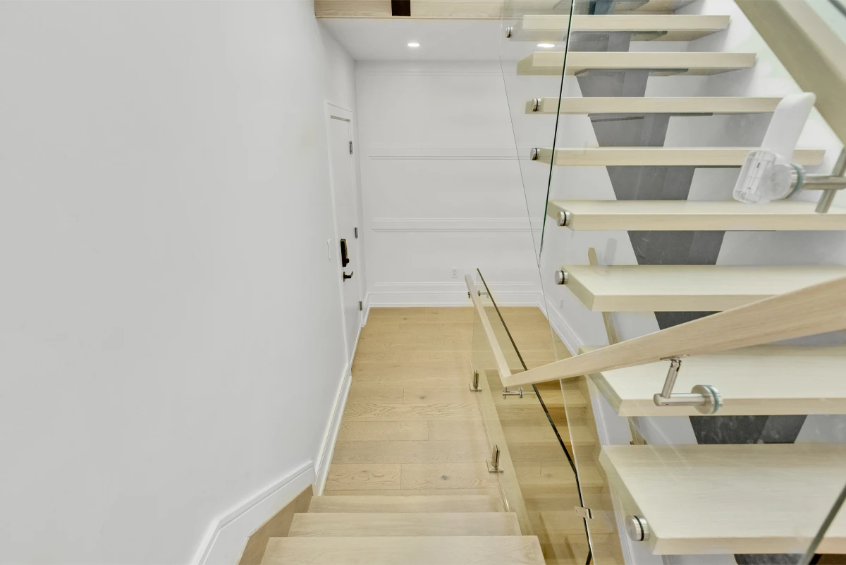 View down the open-tread staircase toward the lower hallway, glass balustrade catching the daylight - RCG Canada
