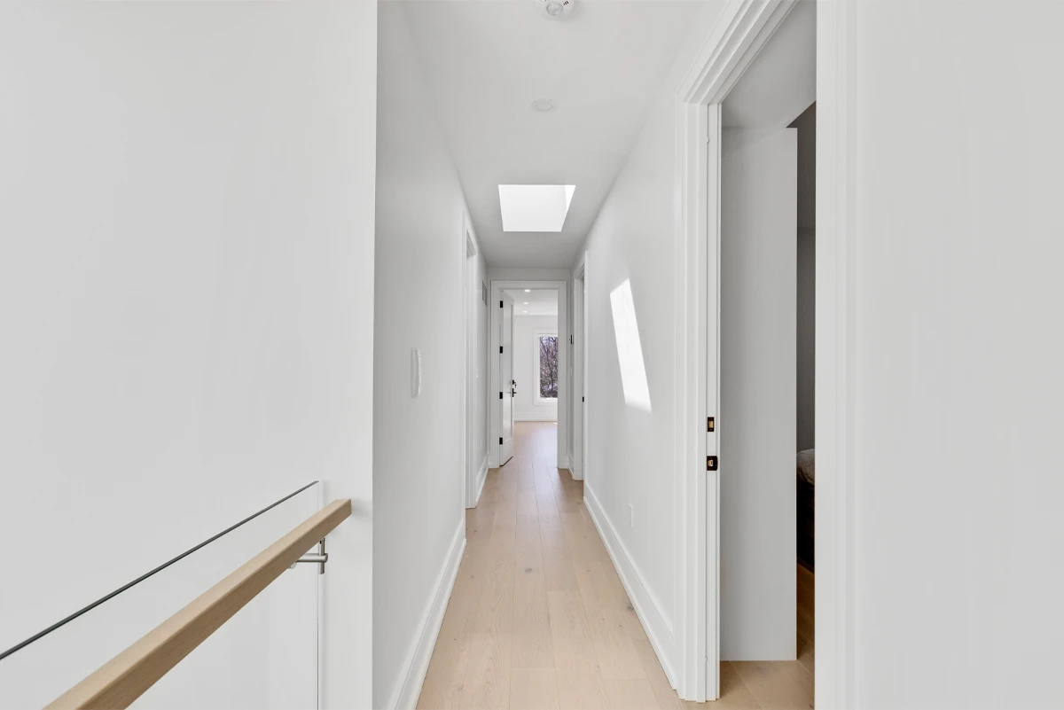 Upper hallway lit by a skylight, leading past bedroom doors to a window at the end in a Mississauga home. RCG Canada interior photography