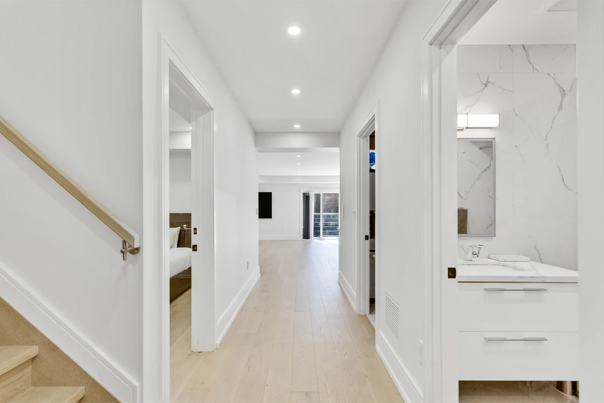 Hallway beside the staircase with a marble-tiled bathroom on one side and the family room ahead - RCG Canada