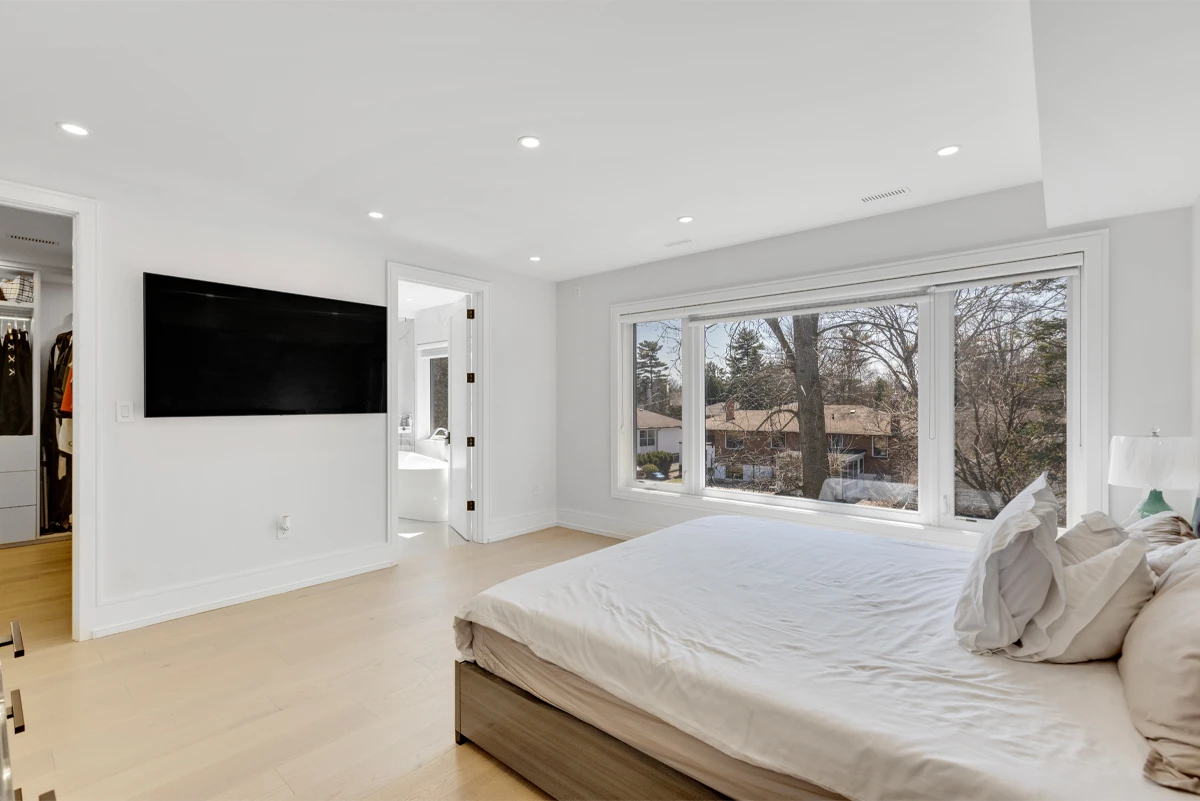 Primary bedroom with a walk-in closet and ensuite doorway beside a wide window over the treetops - RCG Canada