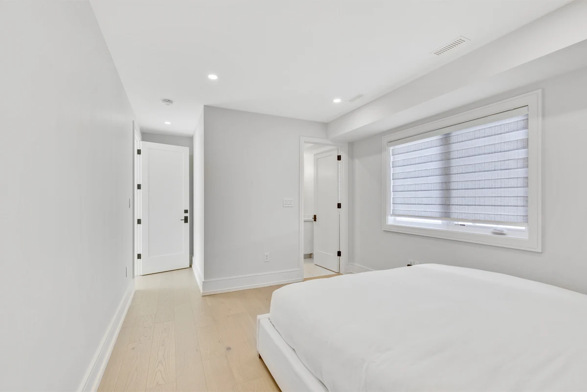 Bright secondary bedroom in crisp white with a corner window, roller blind and its own ensuite doorway in a Mississauga home. RCG Canada interior photography