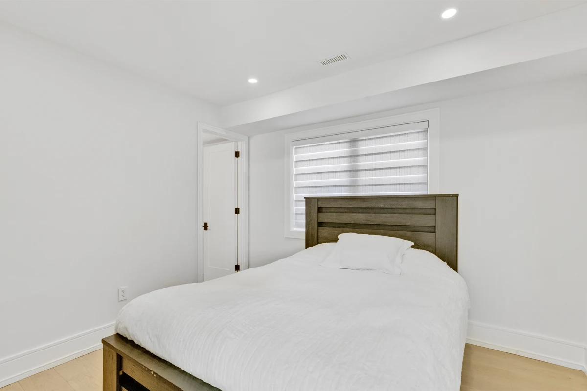 Guest bedroom with a reclaimed-wood headboard set beneath a window with a layered roller blind in a Mississauga home. RCG Canada interior photography