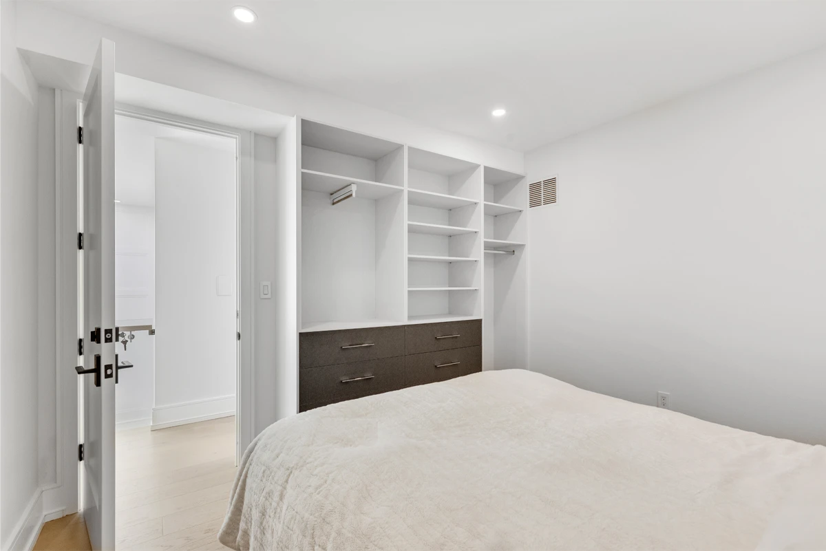 Bedroom with a full wall of built-in open shelving and drawers opening through to the ensuite - RCG Canada