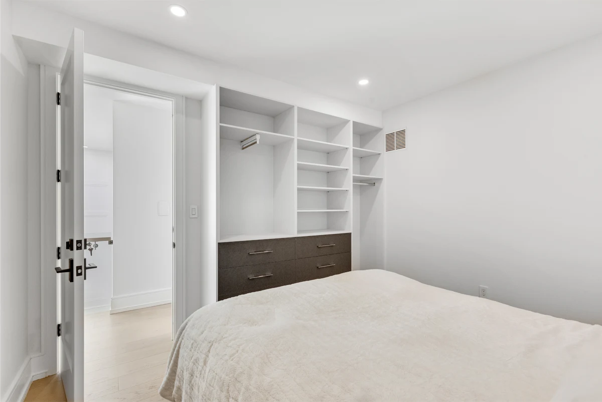 Bedroom with a full wall of built-in open shelving and drawers opening through to the ensuite in a Mississauga home. RCG Canada interior photography