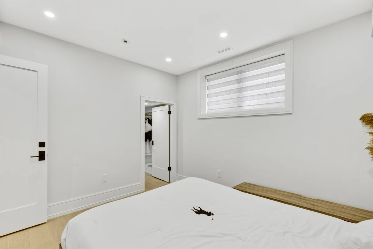 Calm white bedroom with a low platform bed, timber bench and walk-in closet in a Mississauga home. RCG Canada interior photography