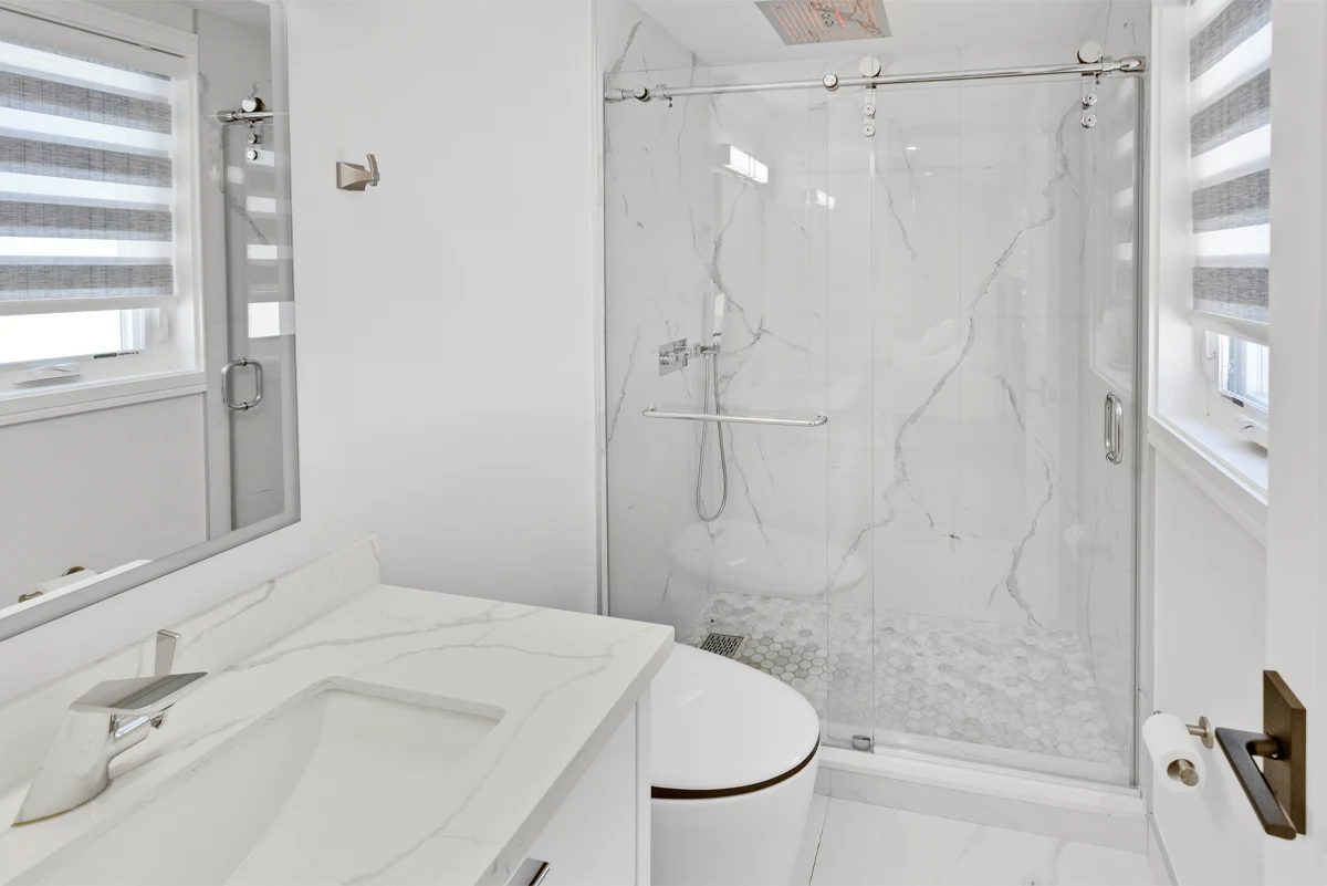 Bathroom with a sliding glass shower enclosure in book-matched marble tile and a quartz-topped vanity in a Mississauga home. RCG Canada interior photography