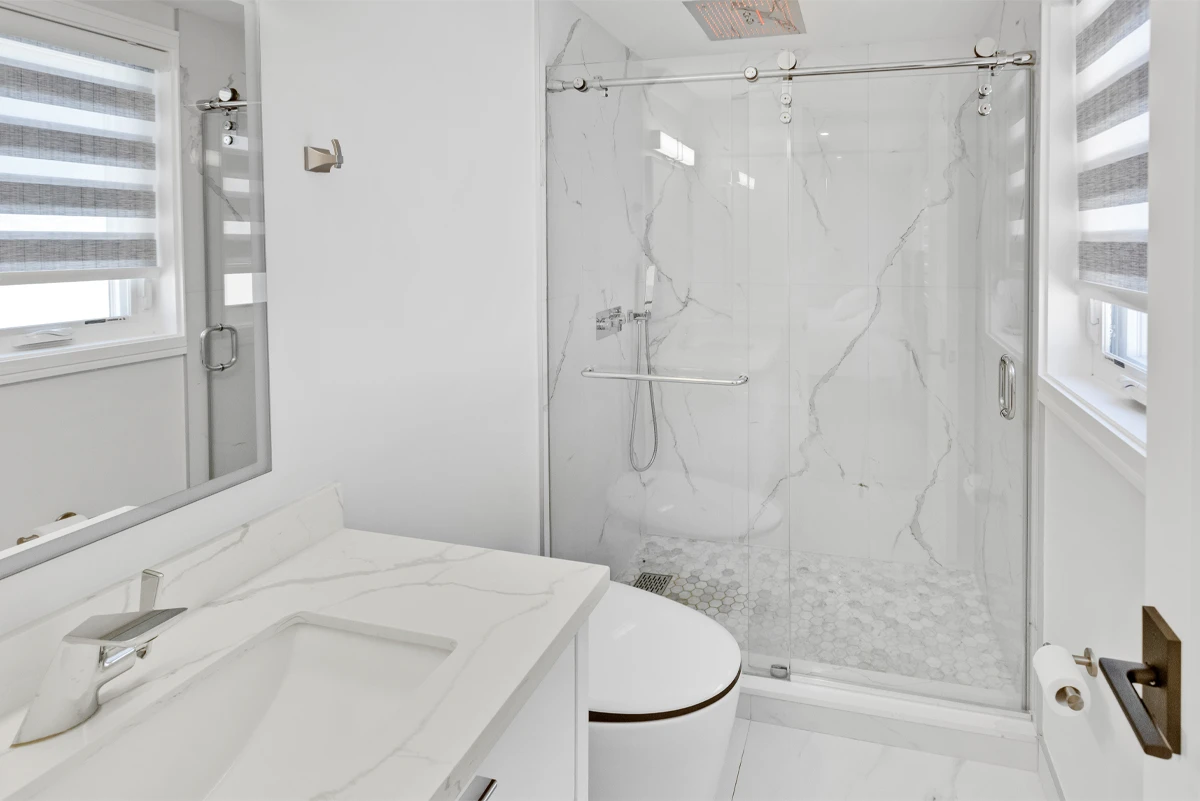 Bathroom with a sliding glass shower enclosure in book-matched marble tile and a quartz vanity - RCG Canada