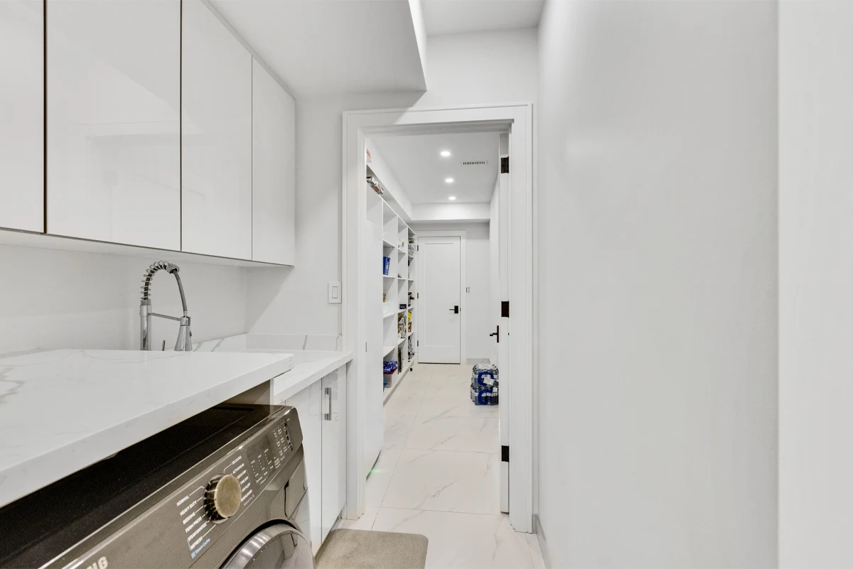 Laundry room with high-gloss cabinetry, a quartz folding counter and utility sink opening onto the walk-in pantry of a Mississauga home. RCG Canada interior photography