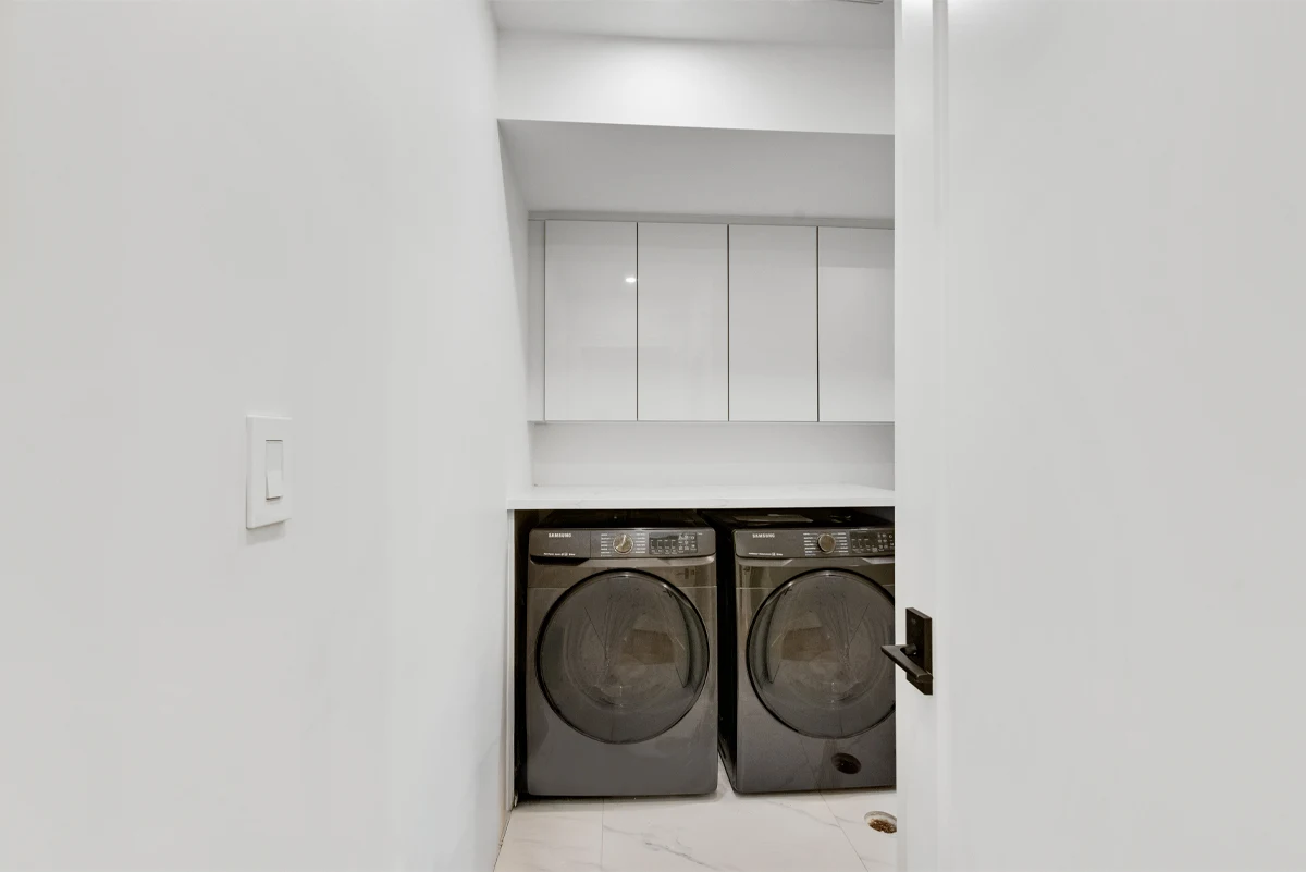 Concealed laundry nook with a side-by-side washer and dryer under a quartz counter and overhead cabinets in a Mississauga home. RCG Canada interior photography