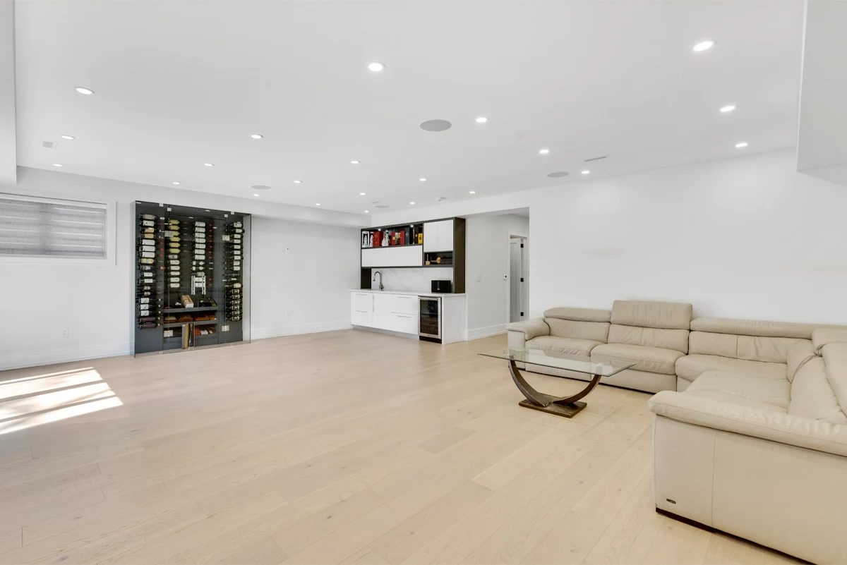 Lower-level lounge with a glass-fronted climate-controlled wine cellar facing a wet bar and leather sectional in a Mississauga home. RCG Canada interior photography